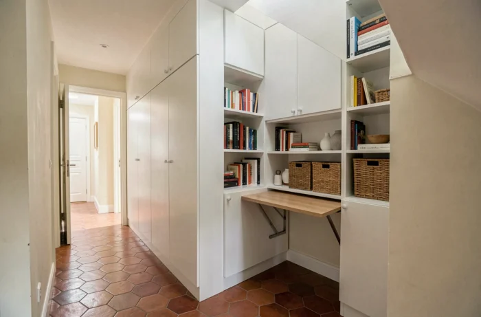 Rangements sur mesure intégrés sous un escalier dans une maison de ville française, exploitant l'espace sous la pente avec bibliothèque et bureau escamotable