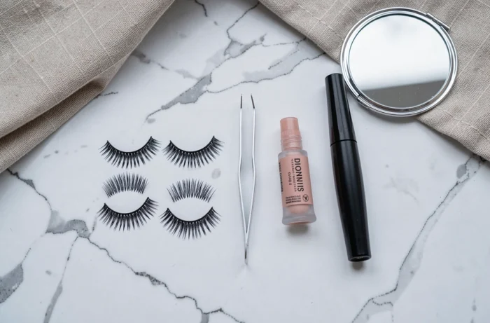 Mise à plat comparant des ricils (faux-cils individuels), de la colle, une pince et un mascara sur surface en marbre blanc